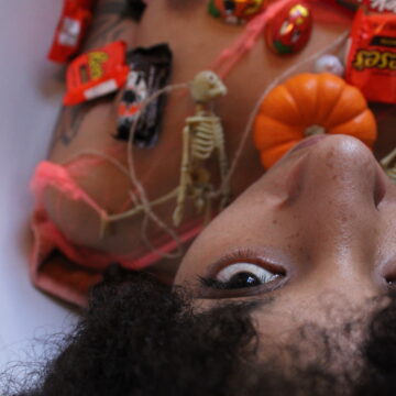 Brook Rain lays with her head toward the camera, covered in mini pumpkins and Halloween Candy