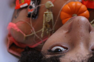 Brook Rain lays with her head toward the camera, covered in mini pumpkins and Halloween Candy