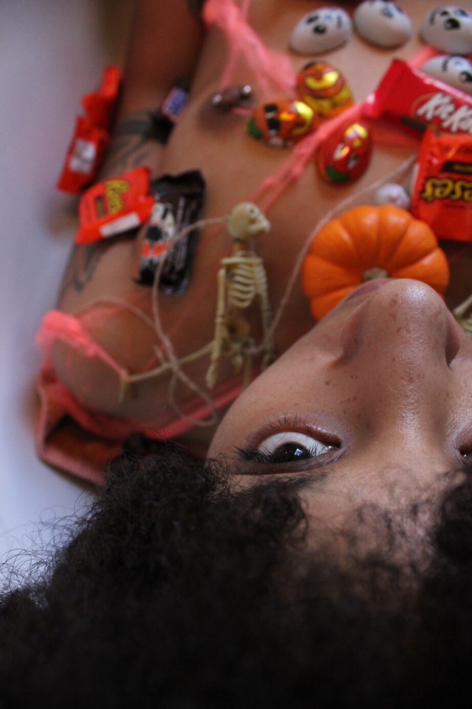 Brook Rain lays with her head toward the camera, covered in mini pumpkins and Halloween Candy